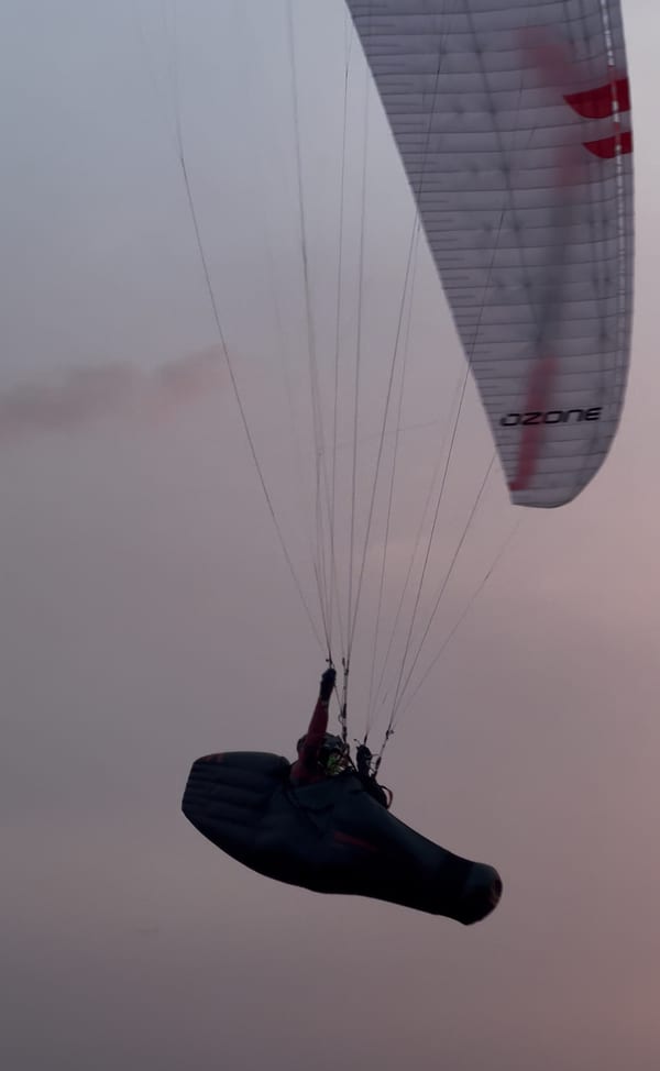 Pilot cruising in pod harness under Ozone wing at magic hour