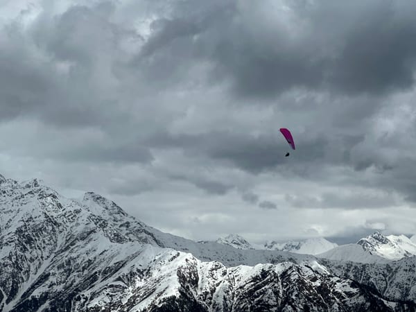 Pink paraglider above moody snow-clad peaks